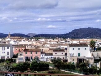 Panoramisch uitzicht op het dorp Sant Llorenç des Cardassar op Mallorca, met traditionele huizen op de voorgrond en bergketens op de achtergrond onder een bewolkte lucht.